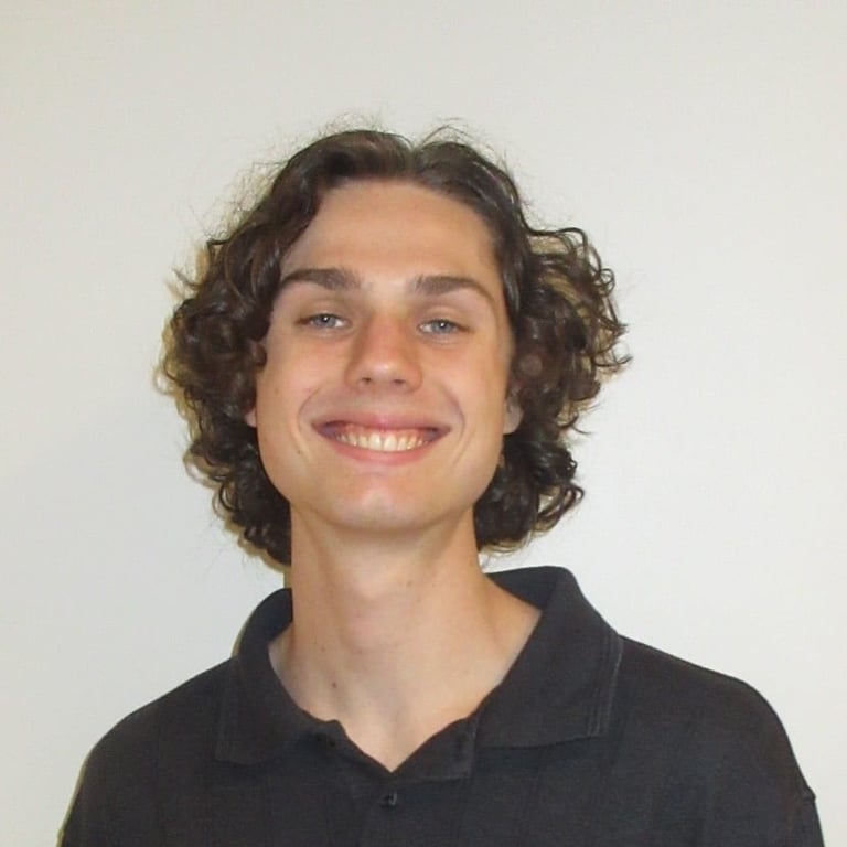 Portrait of a smiling young man with curly dark hair wearing a black collared shirt against a neutral background