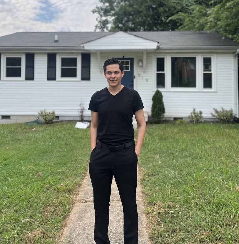 Man in black t-shirt and pants standing on walkway in front of white single-story house with green lawn
