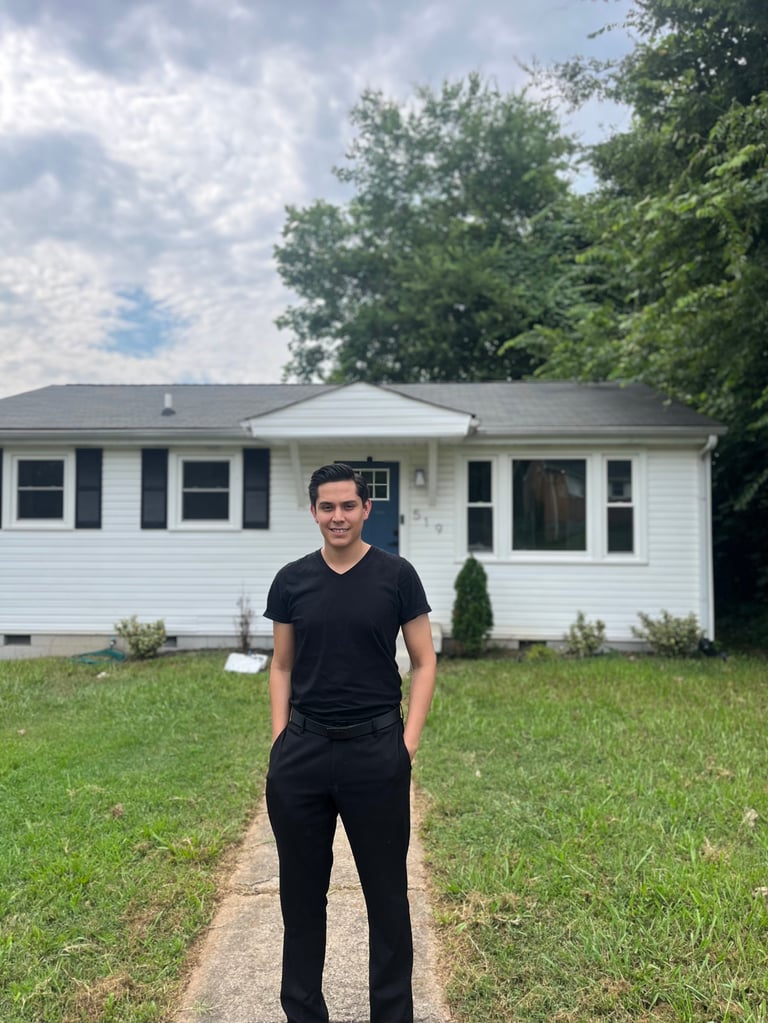 Man in black shirt standing on walkway in front of white single-story house with green lawn and trees