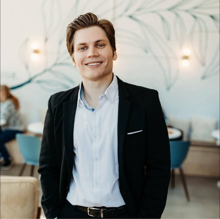 Smiling man in black blazer and light blue shirt standing in modern office with botanical wall art
